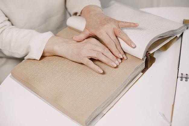 Osoba niewidoma czytająca brajlem, widaćtylko ręce i rozłożoną książkę.